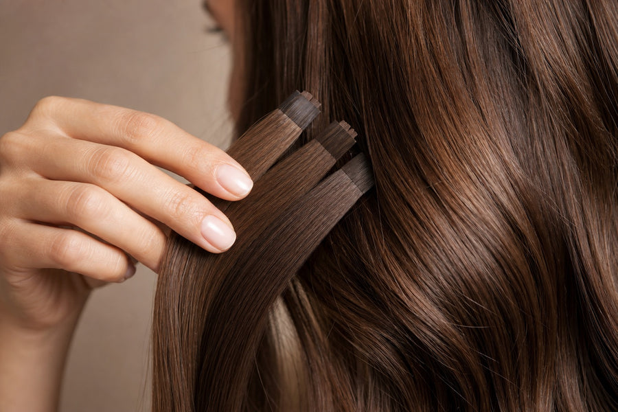 A hand holding human-hair shade swatches against glossy natural hair in daylight to compare color.
